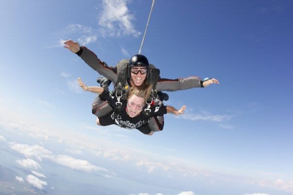 Christine grinning mid-air during a tandem skydive above the clouds